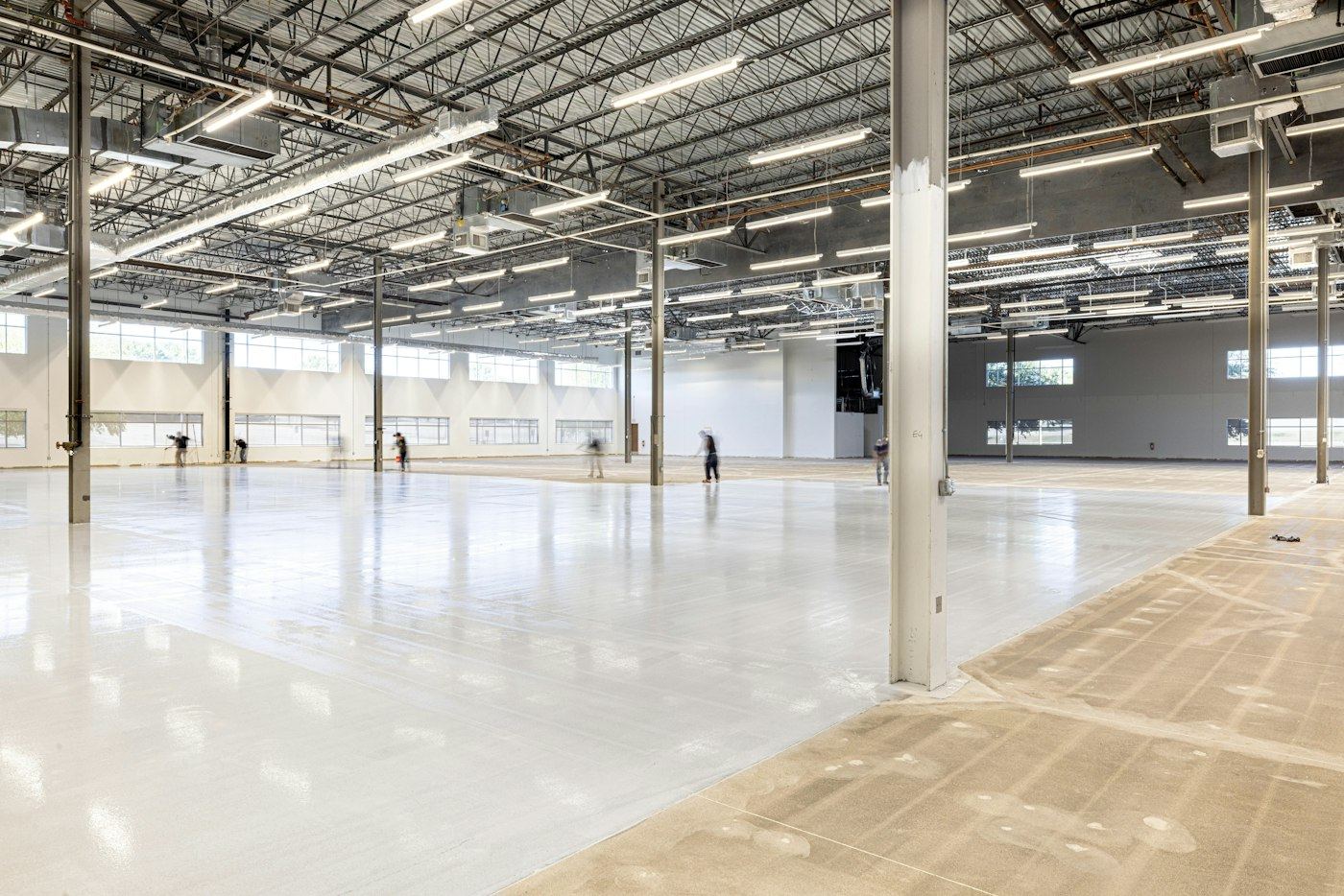 Large shop interior with a glossy light-gray coated concrete floor, steel columns, and an uncoated strip of raw slab on the right. Reference photo, not a completed St. George job.